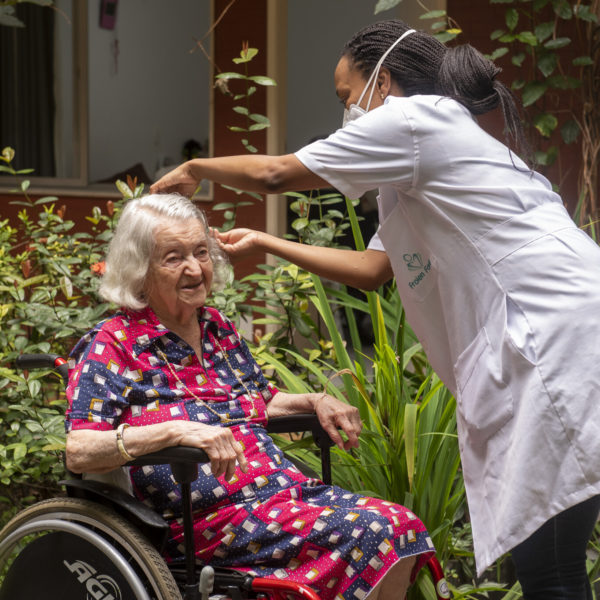 Profissional do Residencial Bem Estar arrumando o cabelo de senhora idosa no jardim